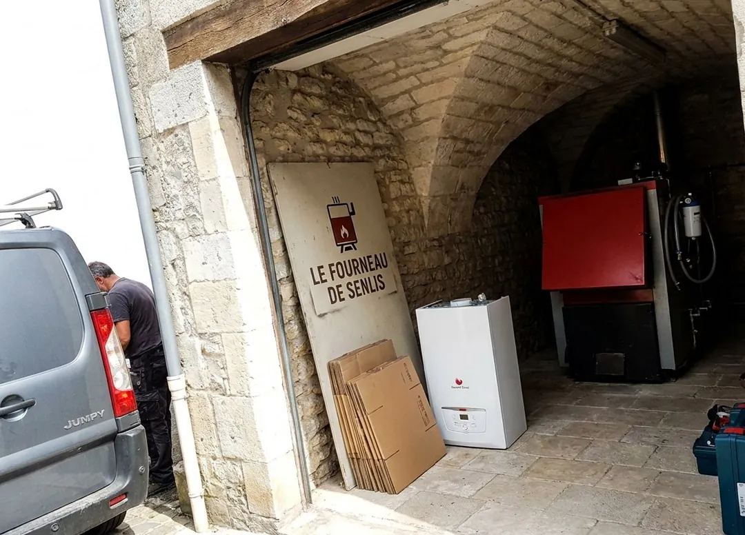Chaufferie sous une voûte en pierre de Senlis : chaudière gaz murale neuve prête à poser et panneau Le Fourneau de Senlis